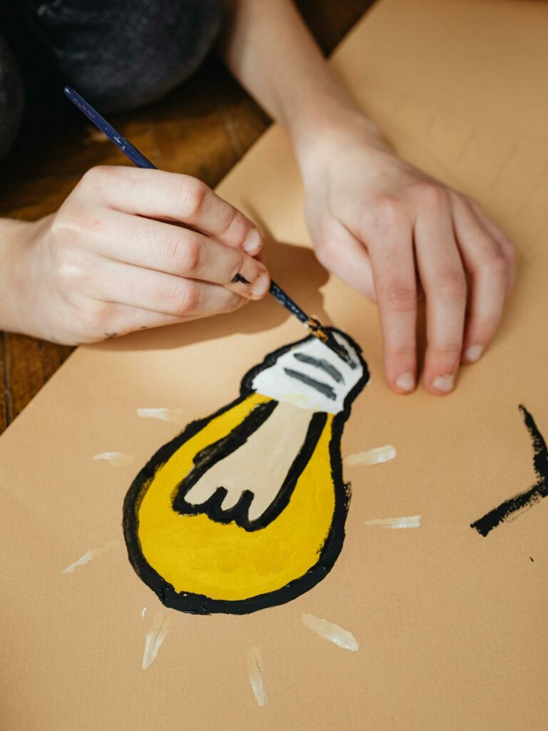 Close-up of hands painting a light bulb on a poster, showcasing creativity and artistic expression.