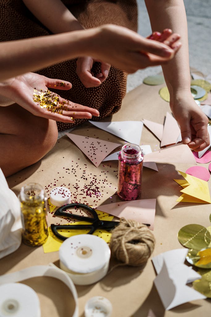 Close-up of hands crafting with colorful paper, glitter, and ribbons; perfect for DIY art projects.
