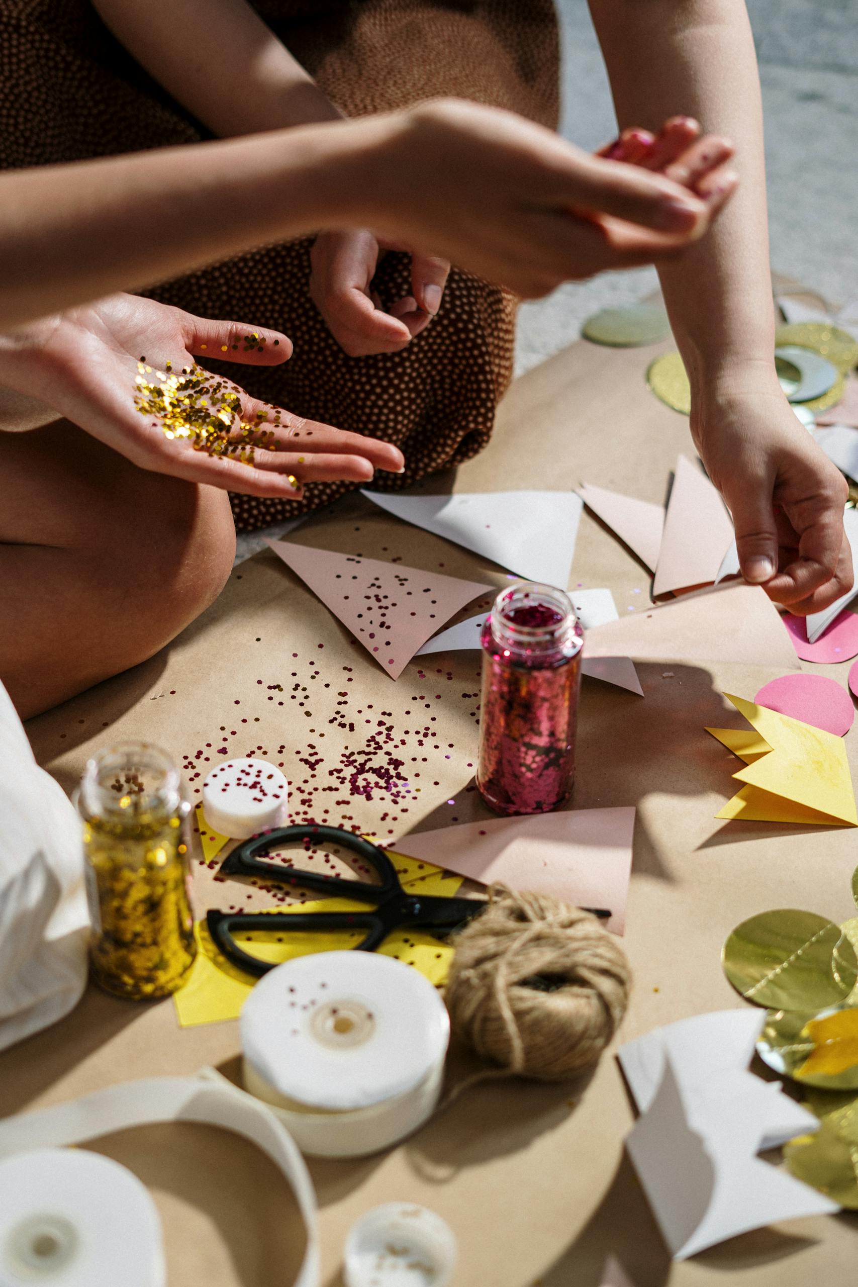 Close-up of hands crafting with colorful paper, glitter, and ribbons; perfect for DIY art projects.